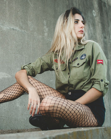 Fashionable young woman in green jacket and fishnet tights posing against urban wall