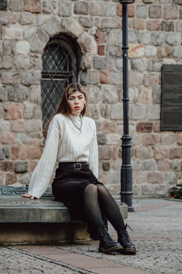 Stylish woman wearing tights and black skirt sitting in front of historic building in winter