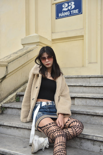 Stylish woman wearing fishnet stockings posing on urban steps in a street fashion outfit