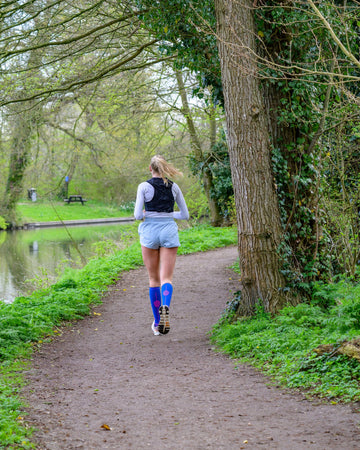 Female runner jogging along a forest trail wearing supportive compression socks for running