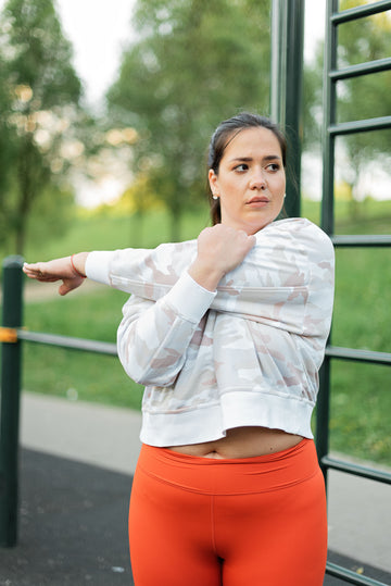 Plus-size woman stretching arms outdoors in park wearing activewear leggings