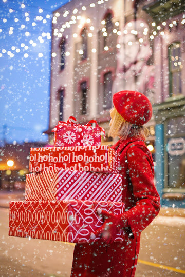 Plus size Black Friday gift guide with a woman carrying stacked wrapped holiday gift boxes