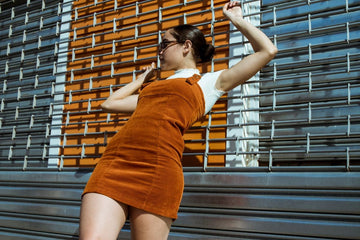 Plus size corduroy overall dress with bib straps worn over a white tee on a city street
