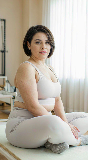 Plus size woman in non-slip grip socks sitting on a yoga mat in a bright pilates studio