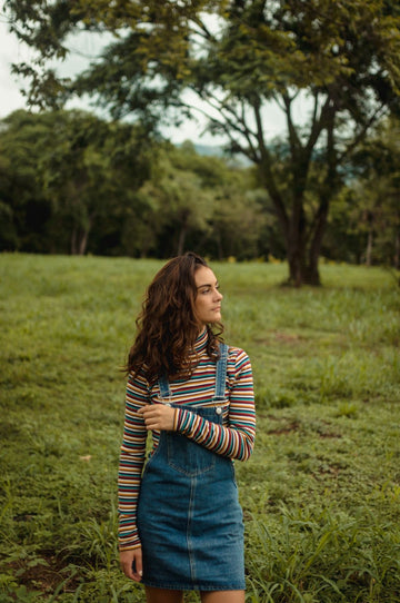 Plus size pinafore dress layered over a striped turtleneck styled in a green meadow