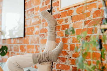 Plus size slouch socks in soft grey knit scrunched on legs propped against a brick wall