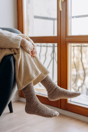 Plus size thermal socks worn by a woman relaxing by a window with a cozy blanket