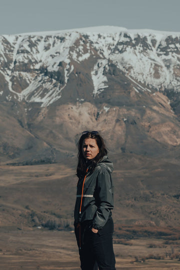 Woman in a plus size windbreaker jacket standing before snowy mountain peaks